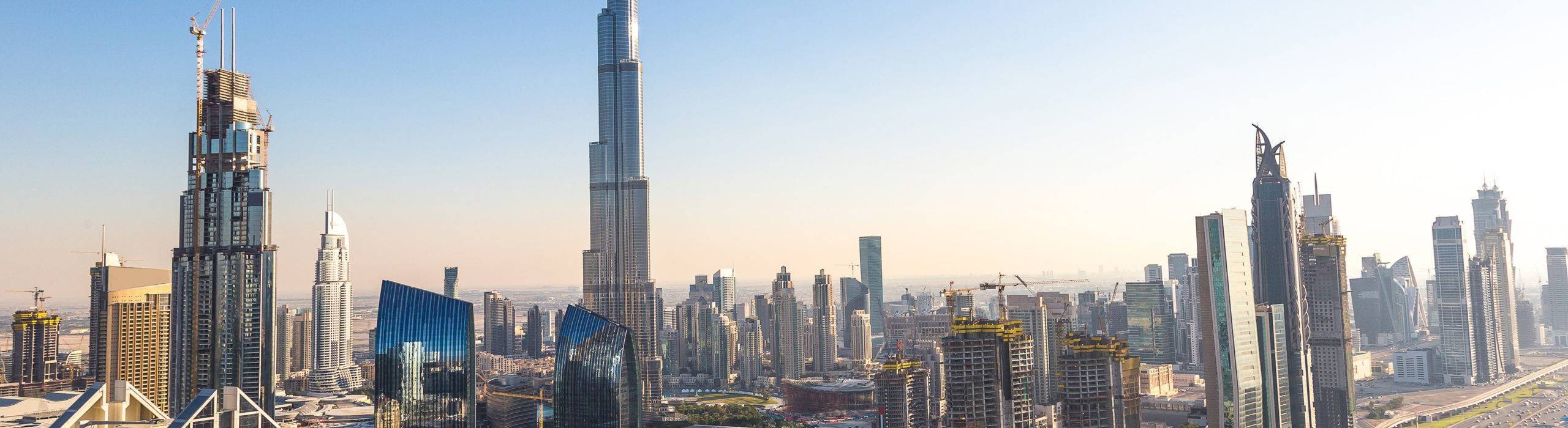 Downtown Dubai skyline with the Burj Khalifa rising above glass towers under a clear sky.