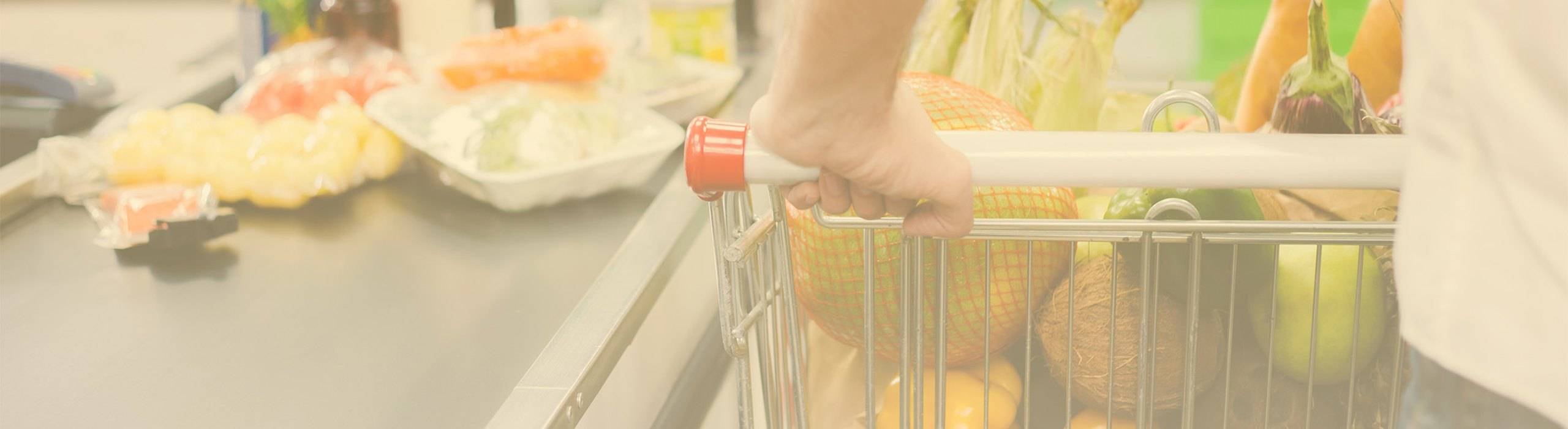 A shopper's hand on the handle of a grocery cart filled with fresh produce at a supermarket checkout