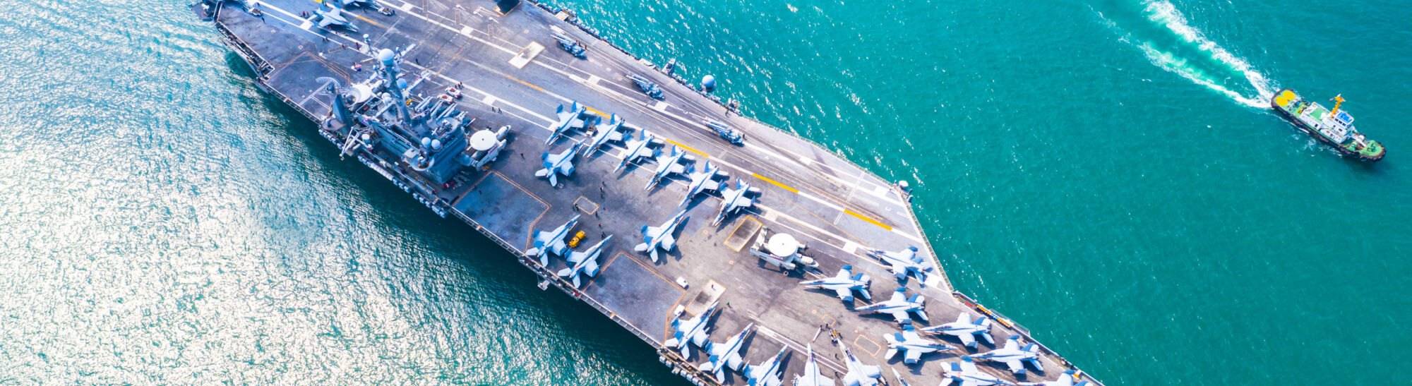 Aerial view of a United States Navy aircraft carrier under way, fighter jets ranged along the flight deck and a support vessel alongside