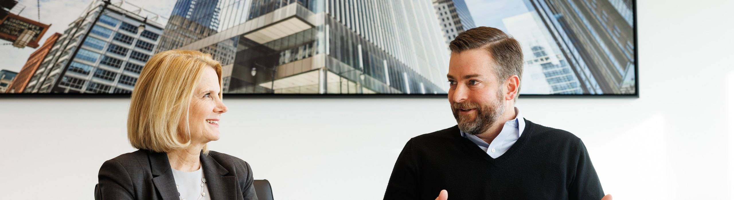 Two Lincoln International valuations professionals in conversation across a conference table beneath a large photograph of city skyscrapers.